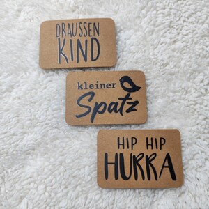 May include: Three brown paper cards with black text and a black silhouette of a bird. The first card says "Draussen Kind". The second card says "kleiner Spatz" with a bird silhouette. The third card says "Hip Hip Hurra".
