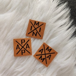 May include: Three brown square patches with black lettering. The patches read "MIN", "PAP", and "MAMA" with the letters arranged in a cross pattern.