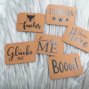 Könnte beinhalten: Sechs braune Geschenkanhänger aus Papier mit schwarzer Beschriftung. Die Anhänger zeigen verschiedene Designs, darunter einen Fuchs, Sterne, eine Hexe, einen Pilz, einen Glücksbringer und das Wort "Boo!"