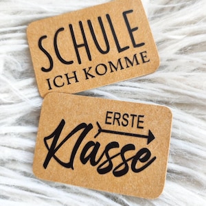 Könnte beinhalten: Zwei braune Papierkarten mit schwarzem Text. Die obere Karte sagt "Schule Ich Komme". Die untere Karte sagt "Erste Klasse" mit einem Pfeil nach rechts.