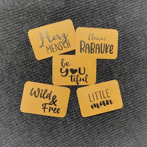 Può includere: Cinque etichette regalo in carta marrone con lettere nere. Le etichette recitano "Herz Mensch", "kleiner Rabaue", "be you tiful", "Wild & Free" e "LITTLE man".