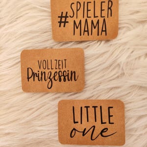 Könnte beinhalten: Drei braune Papieretiketten mit schwarzem Text. Das erste Etikett lautet "#SPIELLER MAMA", das zweite Etikett lautet "VOLLZEIT Prinzessin" und das dritte Etikett lautet "LITTLE one".