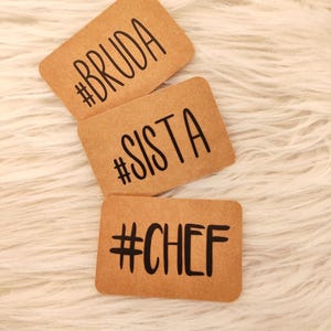 Könnte beinhalten: Drei braune Papierkarten mit schwarzem Text. Die Karten haben die Hashtags #BRUDA, #SISTA und #CHEF.