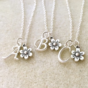 May include: Three silver necklaces with charms. Each necklace has a letter charm and a small flower charm. The letters are A, B, and C.