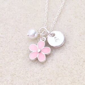 Pu&ograve; includere: Una collana d'argento con un ciondolo a forma di fiore rosa, una perla e un ciondolo a disco d'argento con la lettera 'A' sopra.