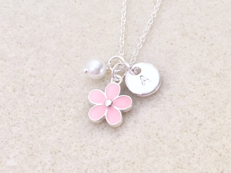Pu&ograve; includere: Una collana d'argento con un ciondolo a forma di fiore rosa, una perla e un ciondolo a disco d'argento con la lettera 'A' sopra.