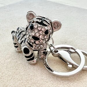May include: A silver and black jeweled tiger keychain with a silver key ring. The tiger is covered in clear and pink rhinestones.