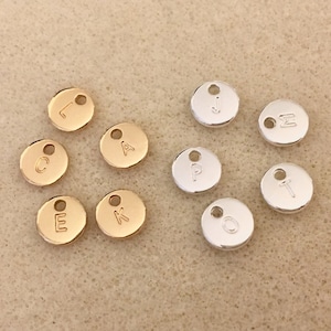 May include: Assortment of gold and silver metal letter charms. The charms are round and have a hole at the top for attaching to a necklace or bracelet. The letters are: L, C, A, E, K, J, &Sigma;, P, T, O.