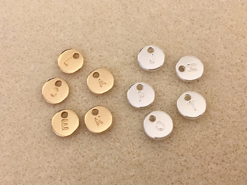 May include: Assortment of gold and silver metal letter charms. The charms are round and have a hole at the top for attaching to a necklace or bracelet. The letters are: L, C, A, E, K, J, &Sigma;, P, T, O.