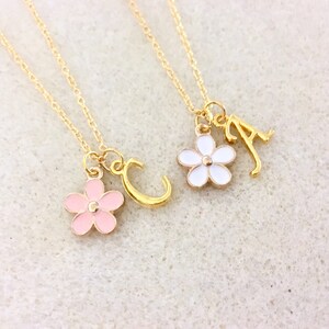 May include: Two gold necklaces with delicate chains and charms. One necklace has a pink flower charm and a gold letter 'C' charm. The other necklace has a white flower charm and a gold letter 'A' charm.