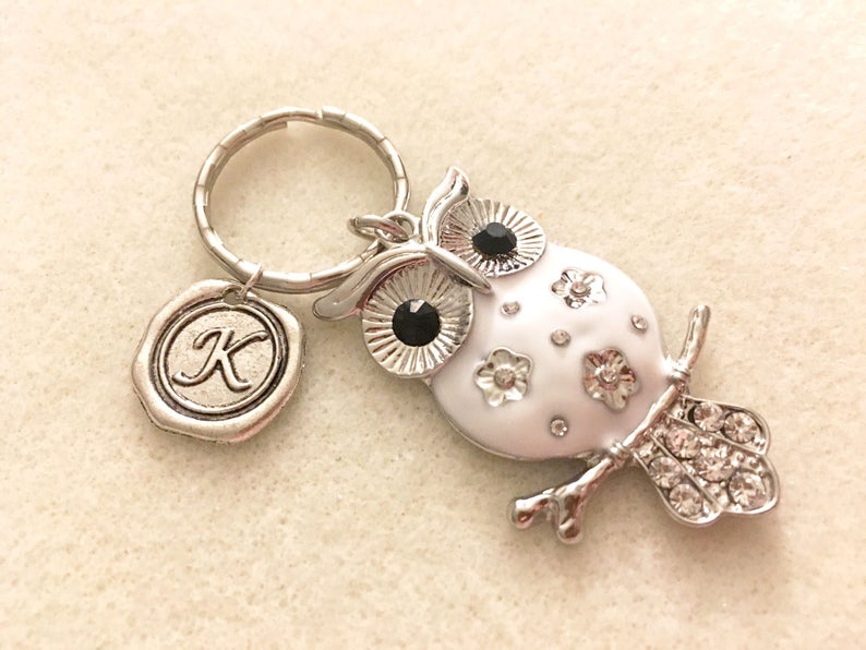 May include: A silver owl keychain with white enamel and black rhinestones. The owl has a small silver charm with the letter "K" on it.