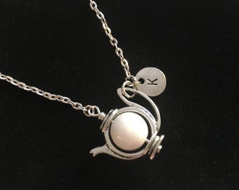 May include: A silver chain necklace with a white teapot charm and a silver charm with the letter "K" on it.