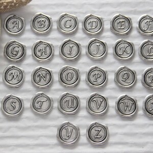 May include: A set of 26 silver-toned metal charms, each featuring a different letter of the alphabet. The charms are circular and have a raised letter design.