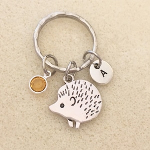 May include: Silver hedgehog keychain with a small amber-colored crystal charm and a silver charm with the letter A.