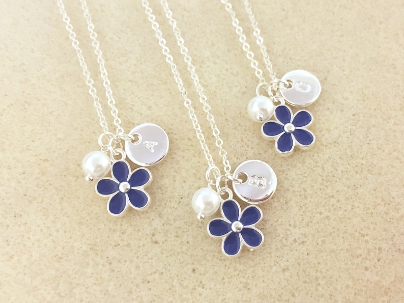 Pu&ograve; includere: Tre collane d'argento con ciondoli a forma di fiore blu, perle e dischi d'argento personalizzati. Ogni disco ha una lettera incisa.