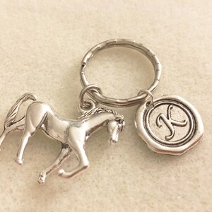 May include: Silver horse keychain with a silver key ring and a silver charm with the letter K.