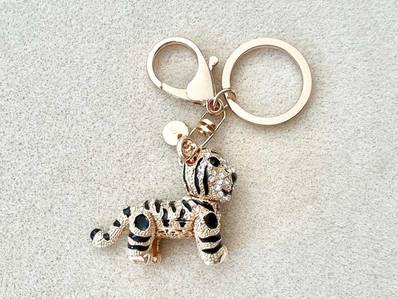May include: Gold-tone key chain with a small, jeweled tiger charm. The tiger is black and white with clear rhinestones.