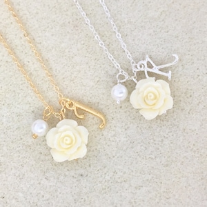May include: Two delicate necklaces with white rose charms and pearl accents. One necklace is gold with a letter 'J' charm, the other is silver with a letter 'K' charm.