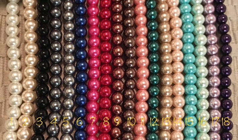 May include: Eighteen strands of pearl beads in various colors, including white, black, gray, blue, pink, red, brown, green, turquoise, and purple. The beads are numbered 1 through 18.