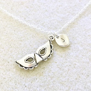 Puede incluir: Collar de plata con un dije de m&aacute;scara de carnaval y un peque&ntilde;o dije inicial. El dije inicial es la letra J.
