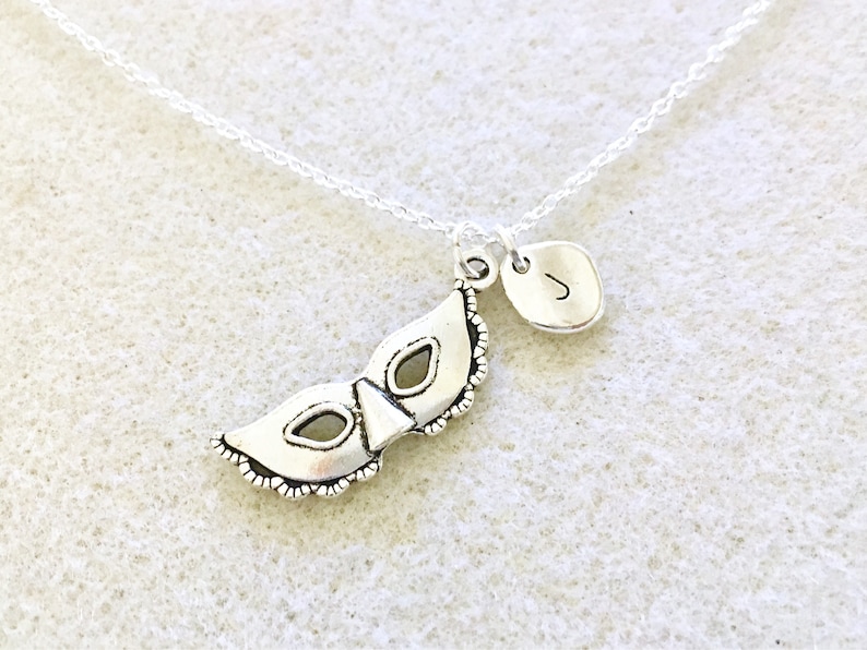 Puede incluir: Collar de plata con un dije de m&aacute;scara de carnaval y un peque&ntilde;o dije inicial. El dije inicial es la letra J.