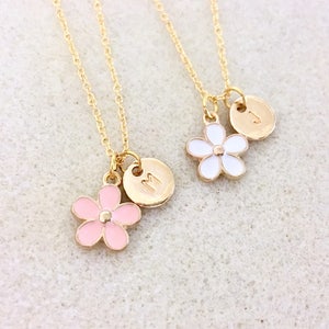 Pu&ograve; includere: Due collane d'oro con catene delicate e ciondoli a forma di fiore. Una collana ha un ciondolo a forma di fiore rosa e un disco d'oro con la lettera "M" su di esso. L'altra collana ha un ciondolo a forma di fiore bianco e un disco d'oro con la lettera "J" su di esso.