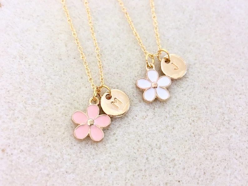Pu&ograve; includere: Due collane d'oro con catene delicate e ciondoli a forma di fiore. Una collana ha un ciondolo a forma di fiore rosa e un disco d'oro con la lettera "M" su di esso. L'altra collana ha un ciondolo a forma di fiore bianco e un disco d'oro con la lettera "J" su di esso.
