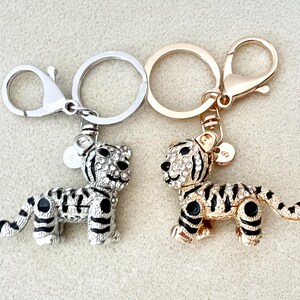 May include: Two silver and gold keychains with tiger charms. The charms are covered in rhinestones and have black stripes.