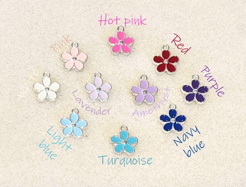 Pu&ograve; includere: Assortimento di 10 ciondoli a forma di fiore in vari colori, tra cui rosa acceso, rosso, viola, lavanda, azzurro, turchese e blu navy. Ogni ciondolo &egrave; un fiore in metallo argentato con un centro in smalto colorato.