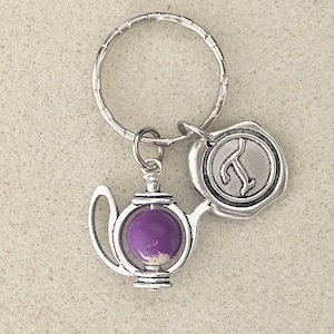 May include: Silver teapot keychain with a purple glass insert and a silver charm with the letter "T" on it.