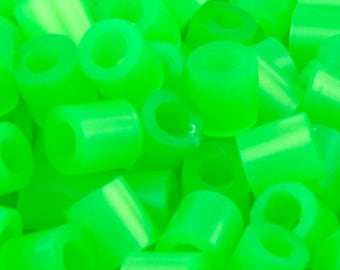 Op de afbeelding: Een close-up van een stapel felgroene plastic kralen. De kralen zijn cilindrisch met een gat in het midden.