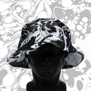 May include: A black and white bucket hat with a marbled pattern. The hat is made of a soft, lightweight fabric and has a wide brim.