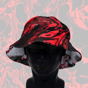 May include: A red and black swirl-patterned bucket hat. The hat is displayed on a black mannequin head against a gray background with a similar swirl design. The hat has a wide brim and eyelets.