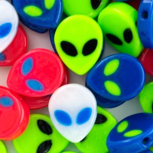 May include: A collection of colorful alien-shaped plastic beads. The beads are in various colors, including green, blue, red, and white. Each bead has a black alien face with two eyes.