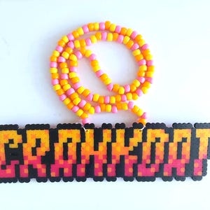 May include: A necklace with the word "GRAHHH" spelled out in pixelated beads. The beads are in shades of orange, yellow, and pink, with a black outline. The necklace chain is made of yellow, pink, and orange beads.