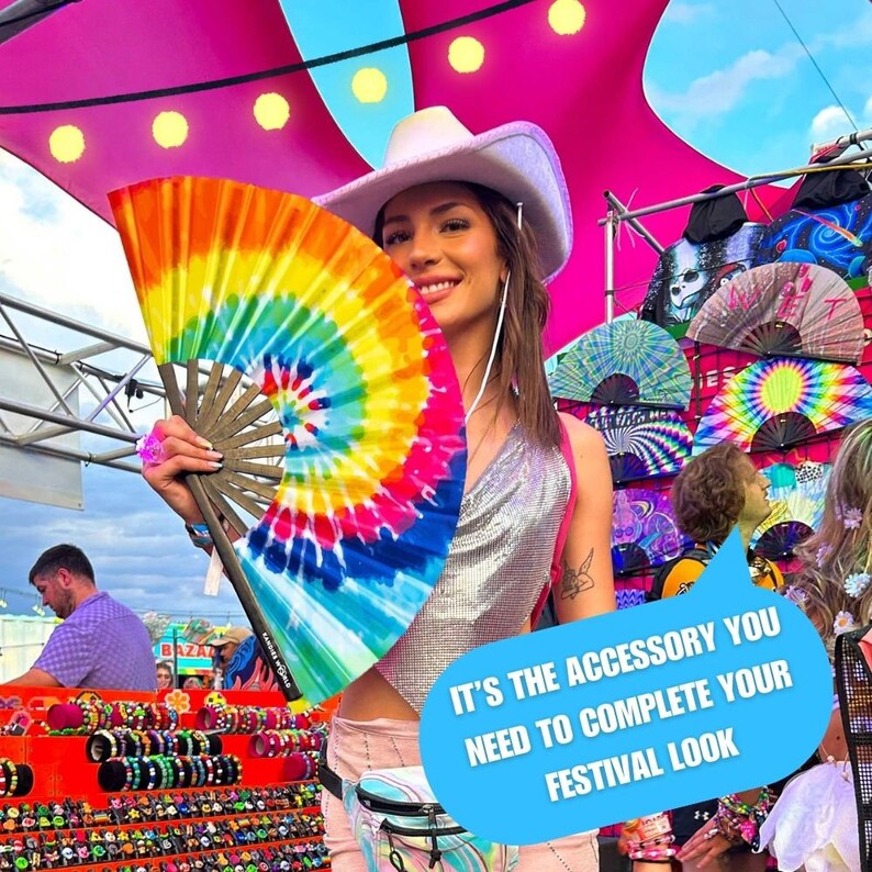 May include: A woman wearing a white cowboy hat holds a rainbow tie-dye hand fan. The fan is made of paper and has a wooden handle. The text "It's the accessory you need to complete your festival look" is in a speech bubble.