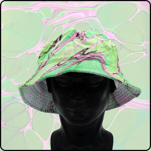 May include: A green and pink bucket hat with a marbled pattern. The hat is made of a soft, comfortable fabric and has a wide brim.