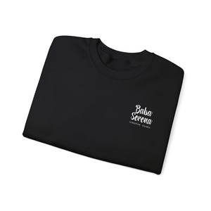 May include: A black crew neck sweatshirt with the white text "Baba Serena creative studio" on the upper left chest. The sweatshirt is folded and appears to be made of a soft material.