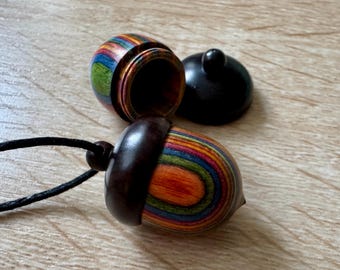 May include: A colorful wooden acorn pendant necklace with a dark brown top and a black cord. The acorn is made of layered wood with stripes of red, orange, yellow, green, blue, and purple.