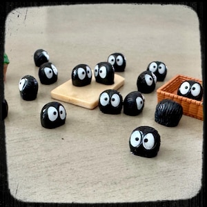 May include: A collection of small black figurines with white eyes. The figurines are arranged on a light brown surface. Some of the figurines are in a small brown basket.