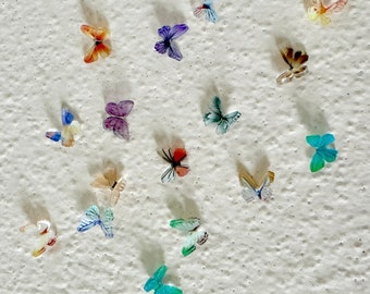 Peut inclure: Une collection de décorations de papillons colorés sur un mur blanc texturé. Les papillons sont en papier et présentent divers motifs et designs.