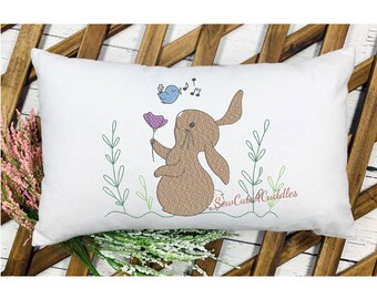 May include: Embroidered pillow featuring a brown bunny with a pink flower, a blue bird, and musical notes. The pillow is white with green stems and leaves. The text "SewCutACuddles" is embroidered in the bottom right corner.