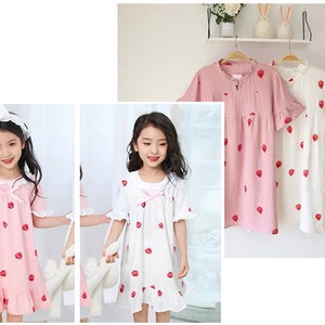 May include: Two girls wearing pink and white strawberry print nightgowns with lace trim. The nightgowns have short sleeves and a ruffled hem.