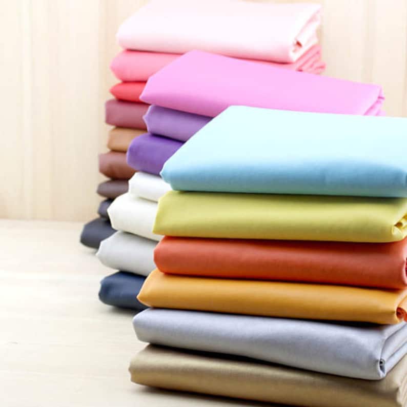 Puede incluir: Una pila de muestras de tela en varios colores, incluyendo rosa, azul, amarillo, naranja y marr&oacute;n. La tela es lisa y parece ser de sat&eacute;n.