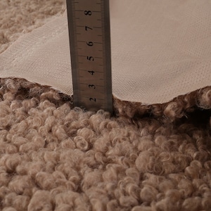 May include: Close-up of a beige faux fur fabric with a ruler measuring 8 inches. The fabric has a curly texture.
