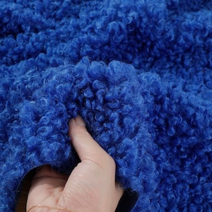 May include: Close-up of a blue, fluffy fabric with a soft, curly texture. The fabric is being held by a hand. The number 21# is visible in the upper right corner of the image.