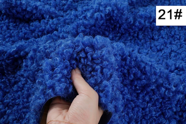May include: Close-up of a blue, fluffy fabric with a soft, curly texture. The fabric is being held by a hand. The number 21# is visible in the upper right corner of the image.