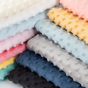 May include: A stack of various colours of soft, textured fabric with a dotted pattern. The colours include white, light blue, pink, yellow, teal, grey, navy blue, and black.