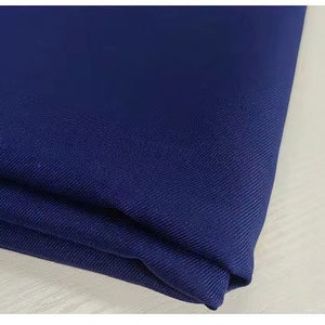 May include: A close-up of a dark blue fabric with a subtle texture. The fabric is folded and appears to be soft and smooth.