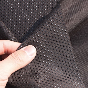 May include: Close-up of brown fabric with a textured pattern of small black dots. The fabric is folded over, showing the underside of the material.